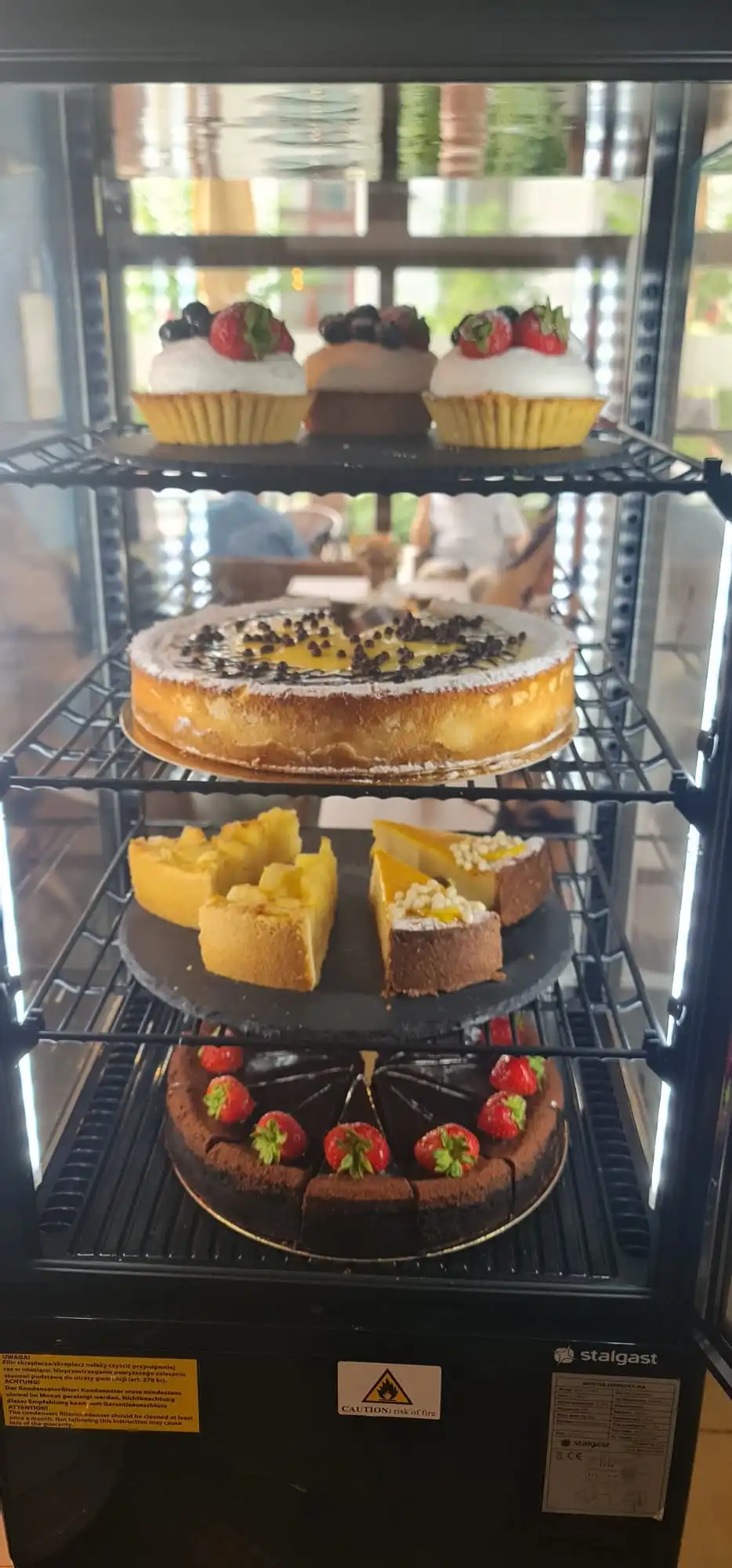 Cake display fridge with cupcakes, tarts and cakes, portrait.