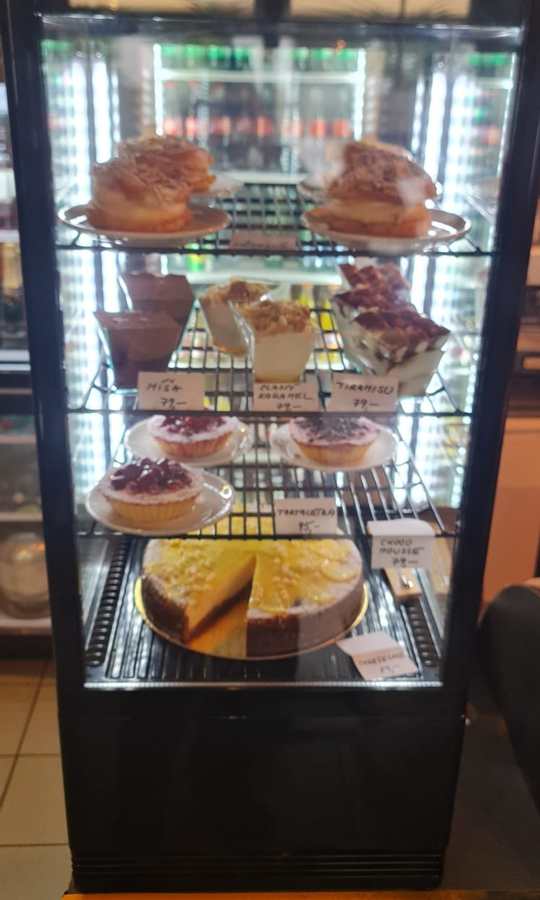 Glass cake display fridge with cheesecakes and cakes, portrait.