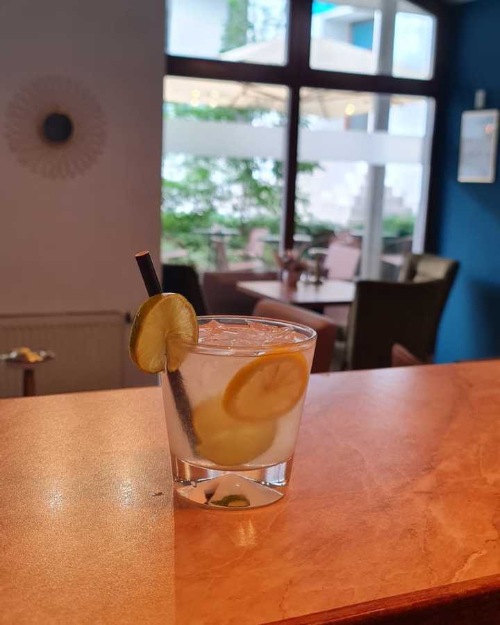 Gin and tonic tumbler on the bar counter under an arched window with courtyard light.