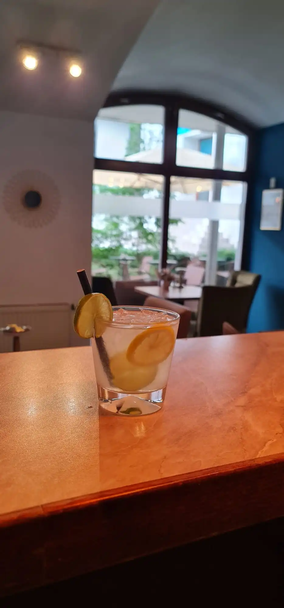 Gin and tonic tumbler on the bar counter under an arched window with courtyard light.