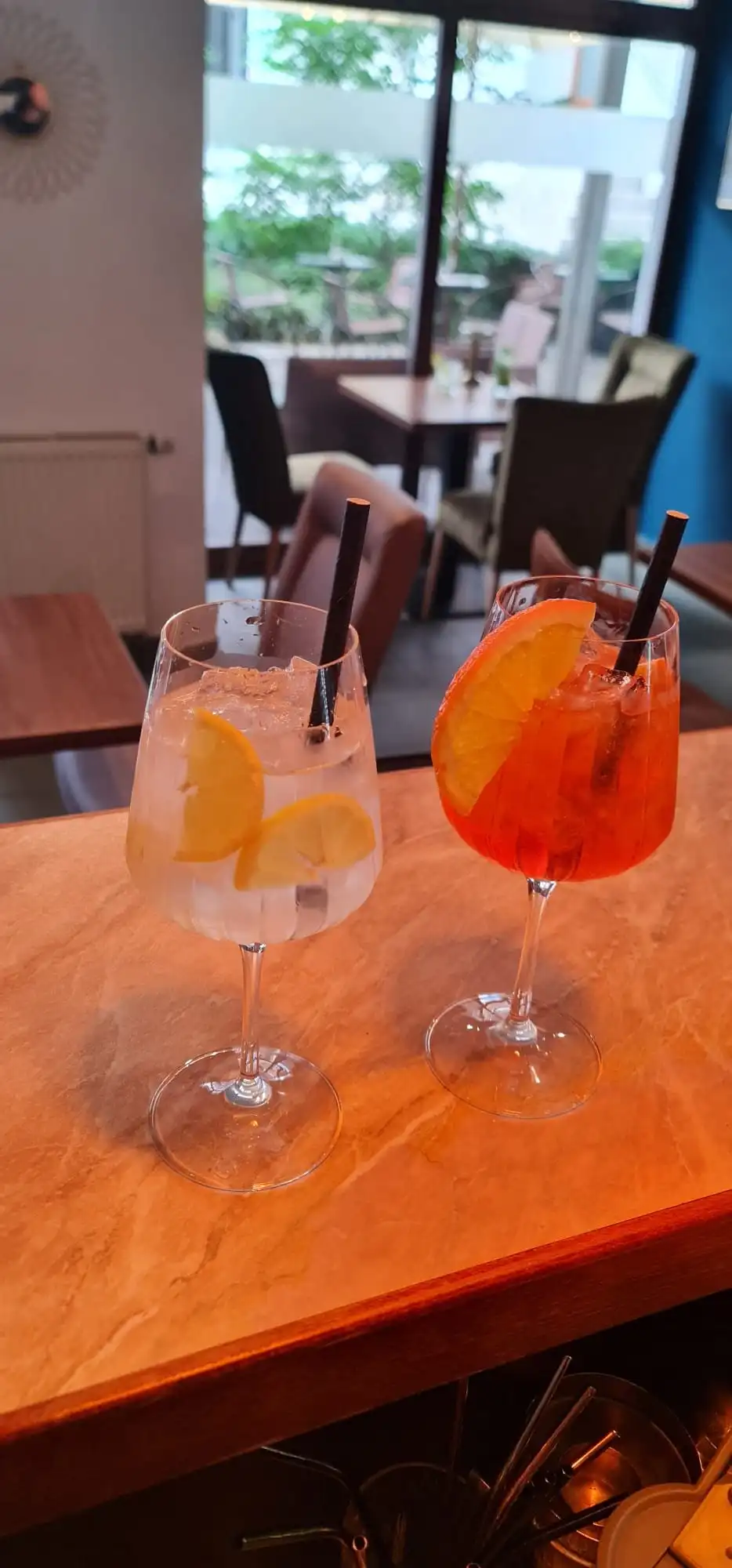 Gin and tonic and Aperol Spritz on the marble-look bar counter, window with courtyard greenery behind.