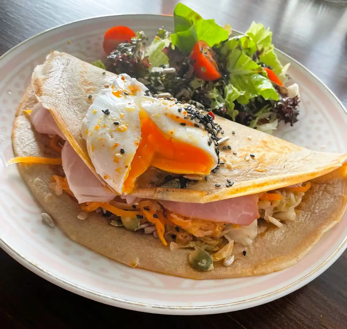 Buckwheat crepe folded over ham, kimchi and a poached egg with sesame, salad on the side.