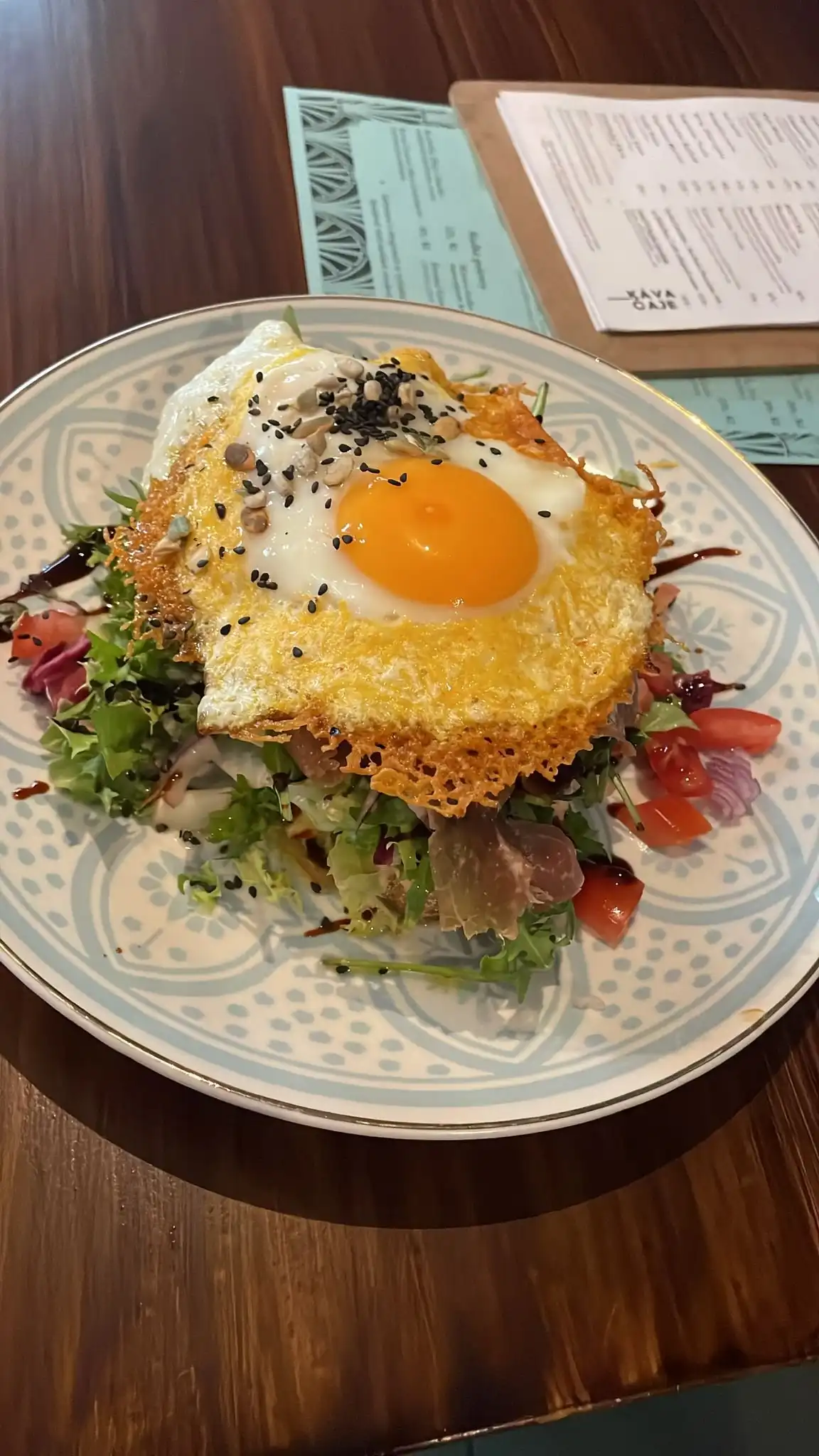 Cheddar egg bread: fried egg on a crispy cheddar crust with salad, tomato and sesame on a pale patterned plate.