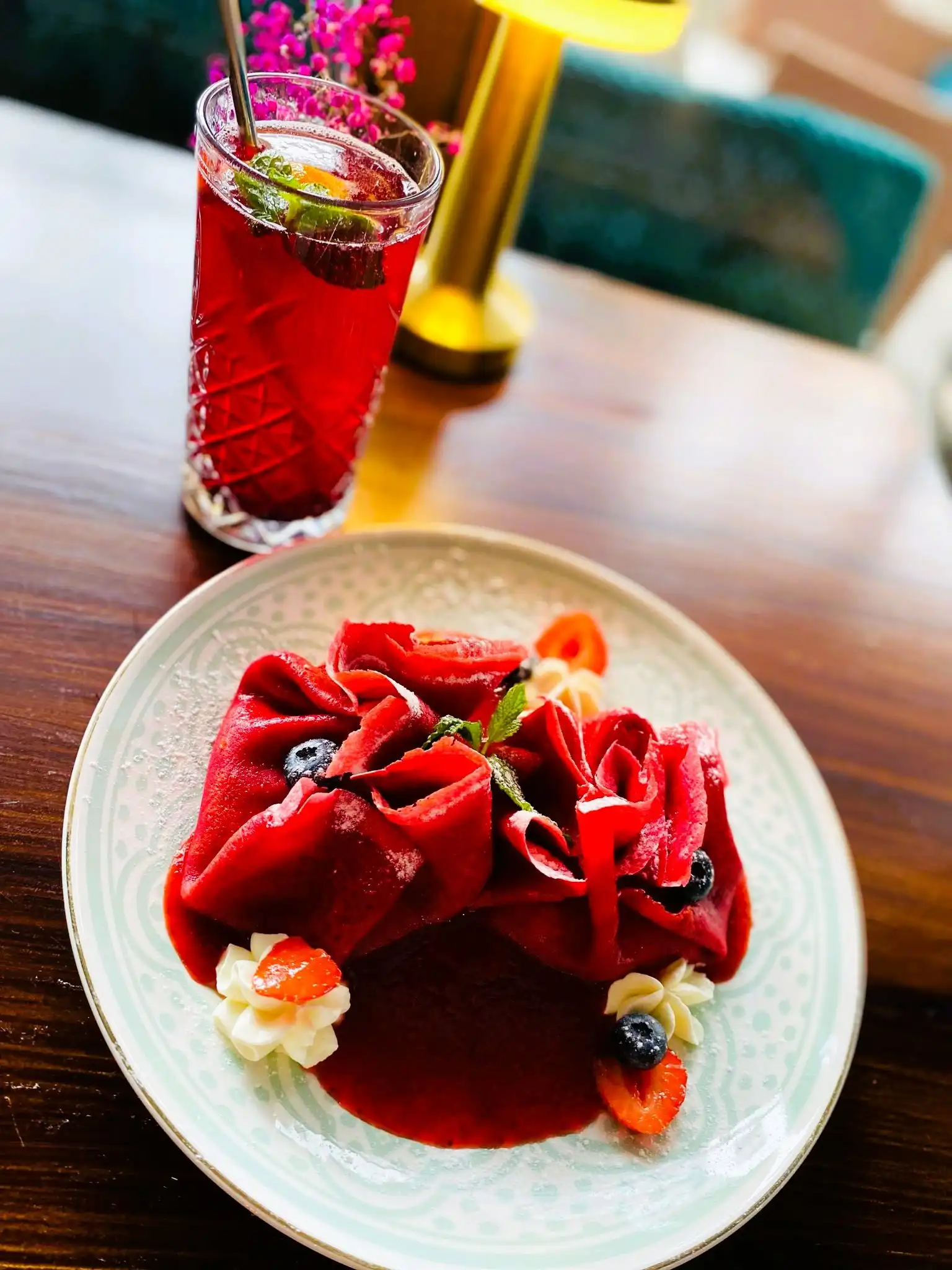 Ruby crepe: deep red beetroot crepe folded around mascarpone cream with strawberry sauce, a red drink with a straw behind.