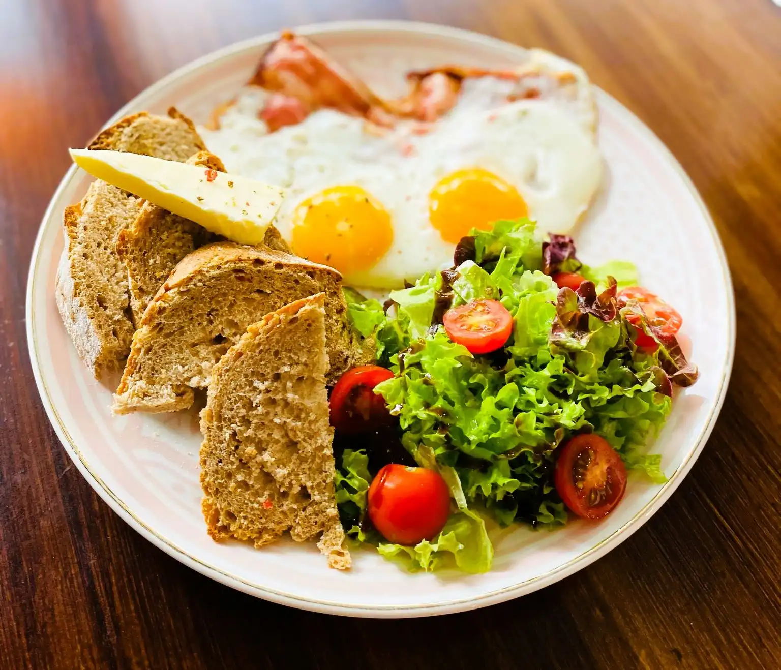 Two sunny side up eggs with bacon, sourdough with butter and salad.