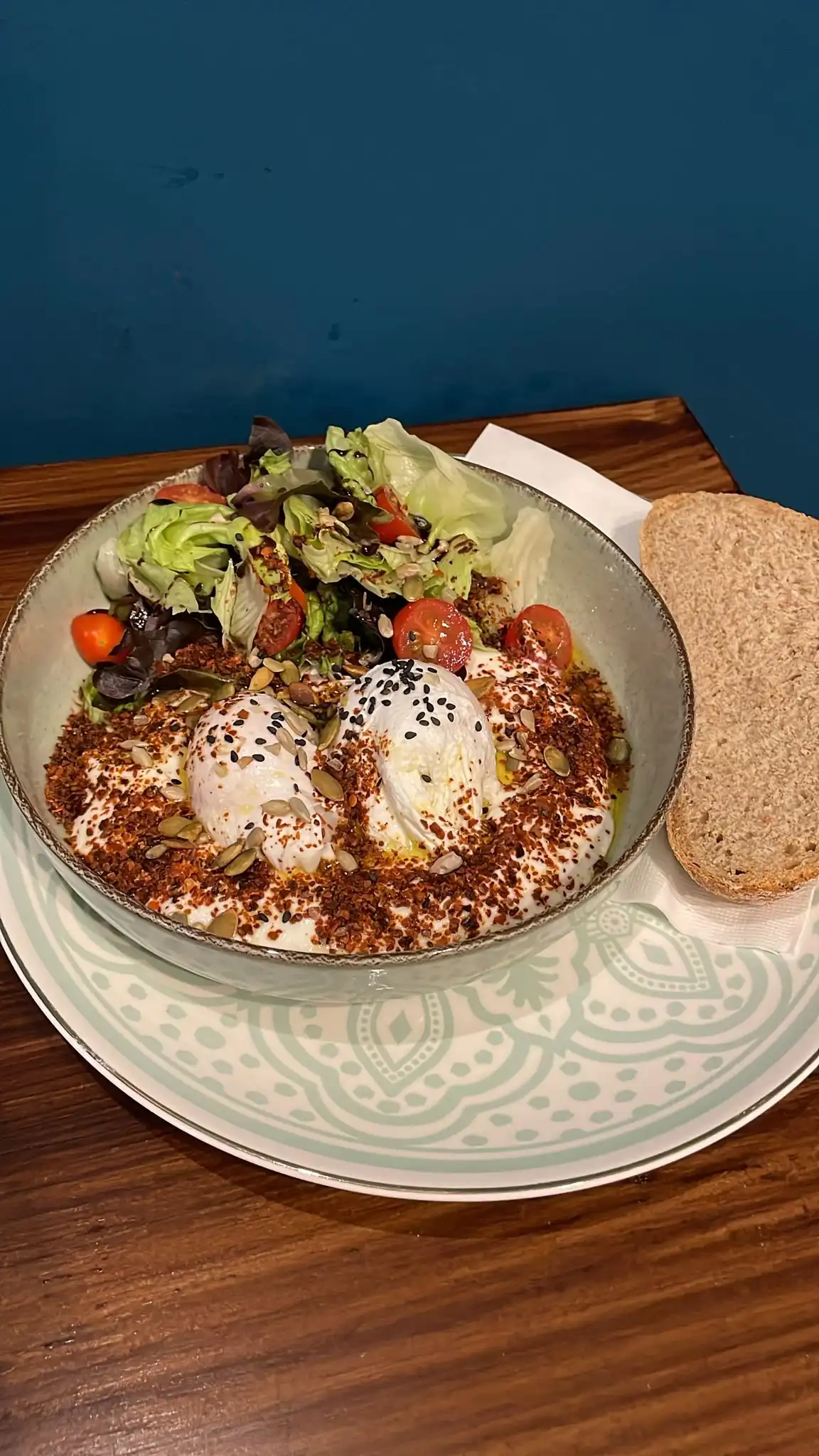 Turkish eggs: poached eggs on garlic yoghurt with chilli butter crumbs, salad on top, sourdough on the side.